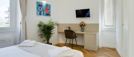 Habitación de hotel con cama, escritorio, silla, televisor, planta y ventana.