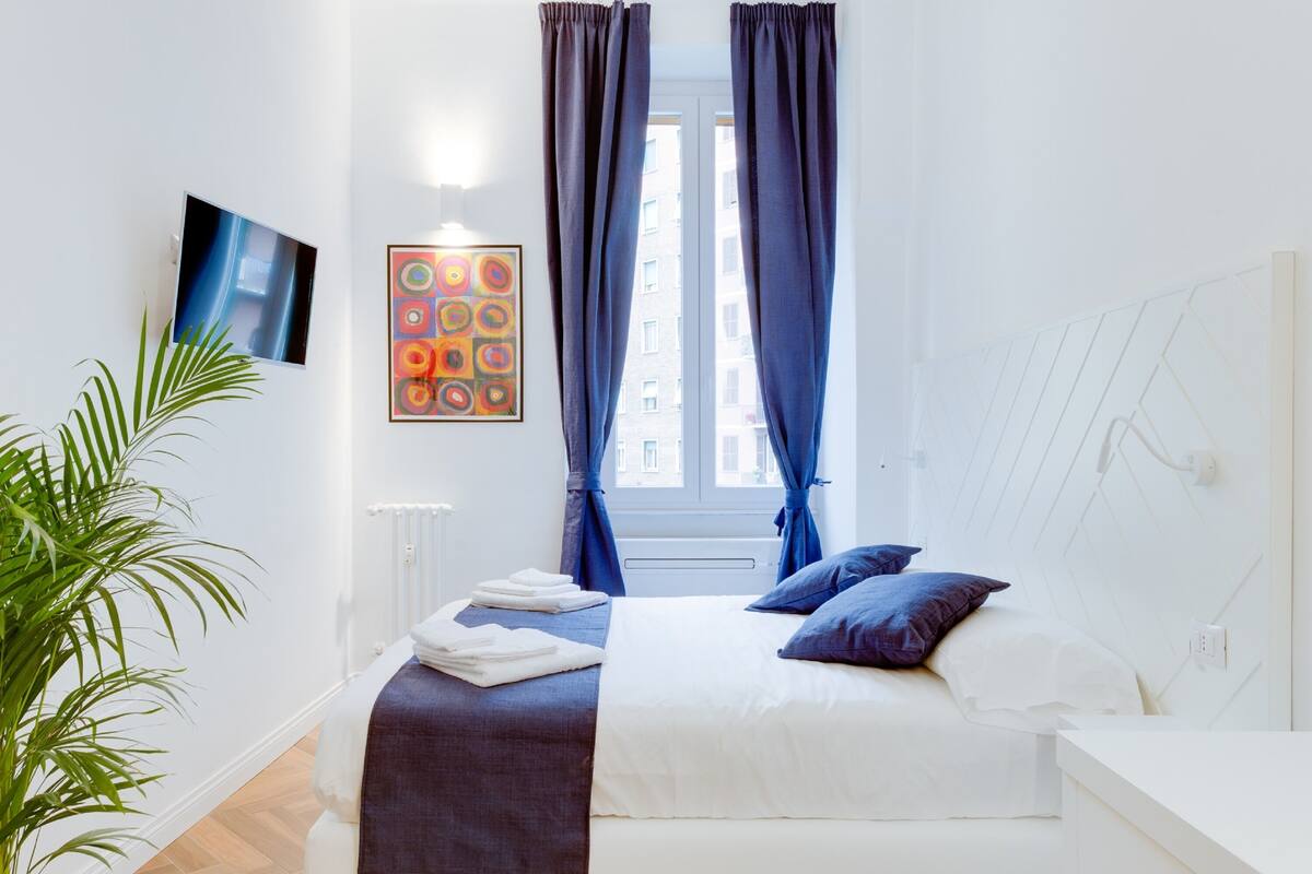 Una camera da letto moderna con un letto, una pianta in vaso, un quadro e una finestra con tende.