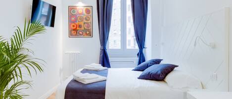 Une chambre moderne avec un lit, une plante en pot, un tableau et une fenêtre avec des rideaux.