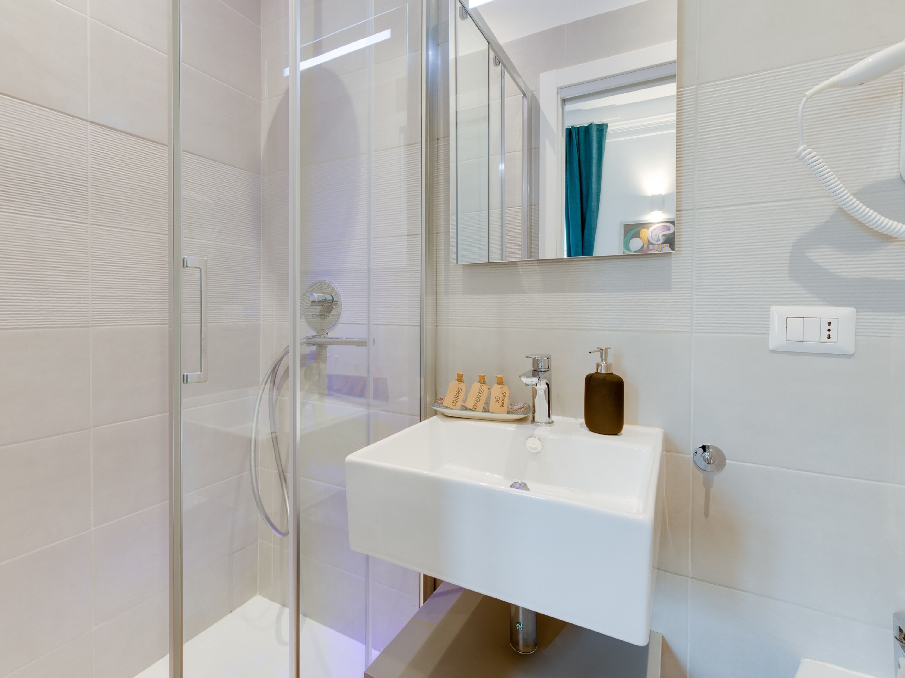 A modern bathroom with a glass shower enclosure, a white sink with a soap dispenser, and a mirror above the sink.