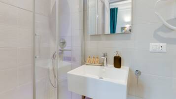 A modern bathroom with a glass shower enclosure, a white sink with a soap dispenser, and a mirror above the sink.