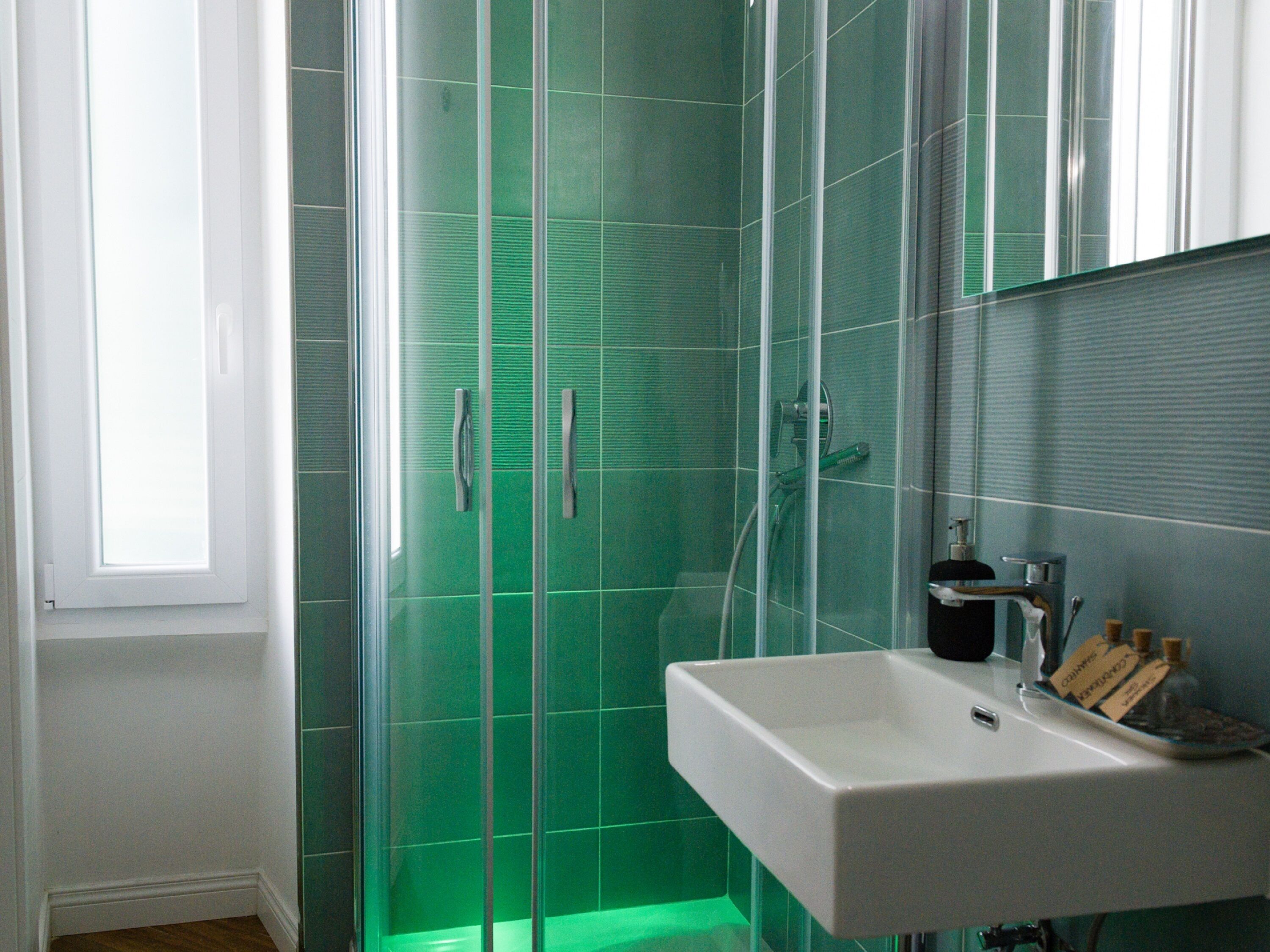 Un baño con cabina de ducha de vidrio, un lavabo blanco y un espejo encima.