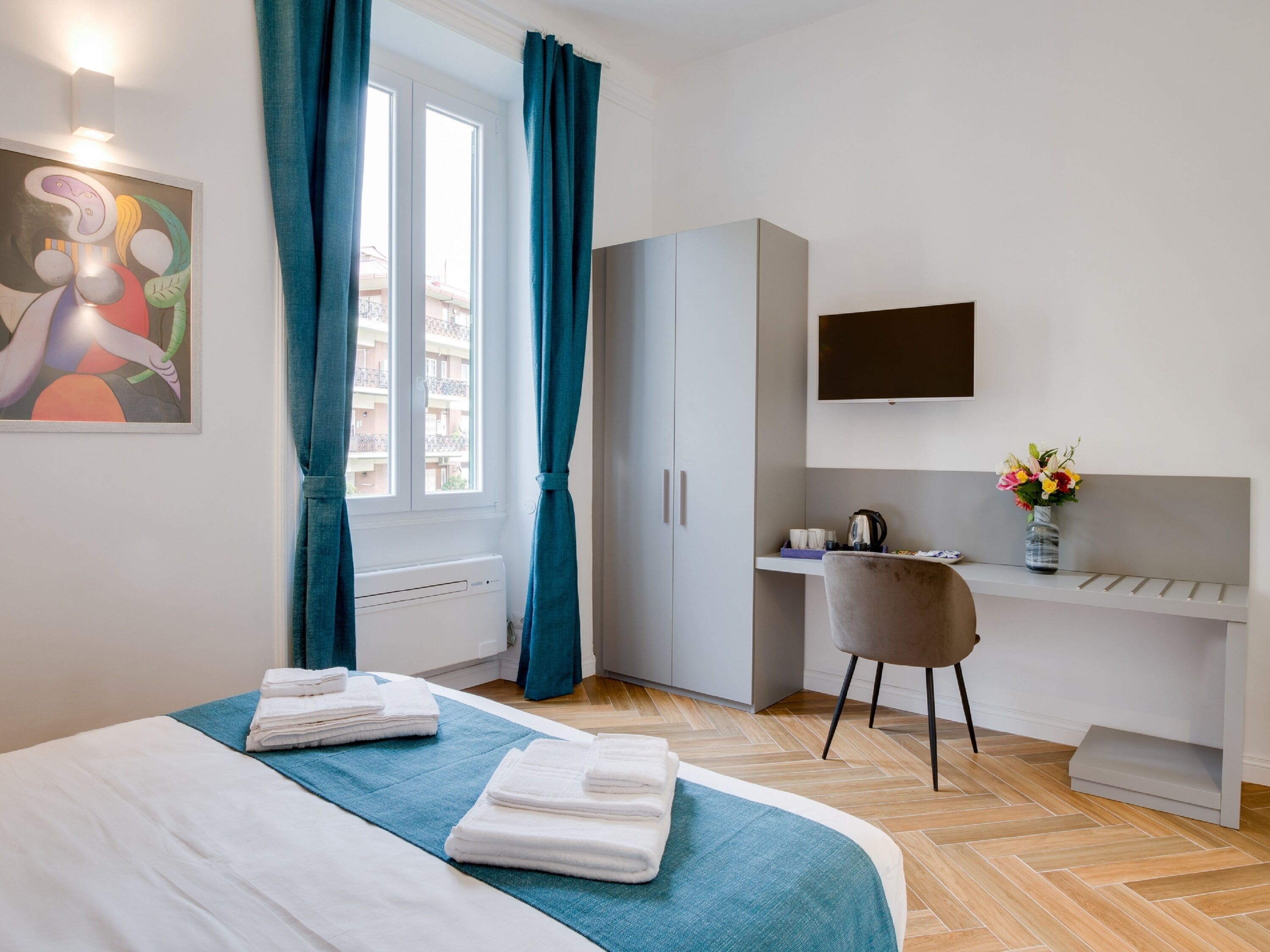 Una camera d'albergo con un letto, una scrivania, una sedia, una televisione e una finestra con tende.