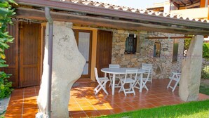 Un patio cubierto con pared de piedra, puertas de madera y mobiliario exterior blanco.