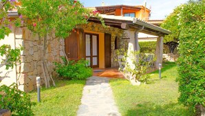 Una casa de piedra con puerta de madera, un sendero de piedra y un jardín con diversas plantas.