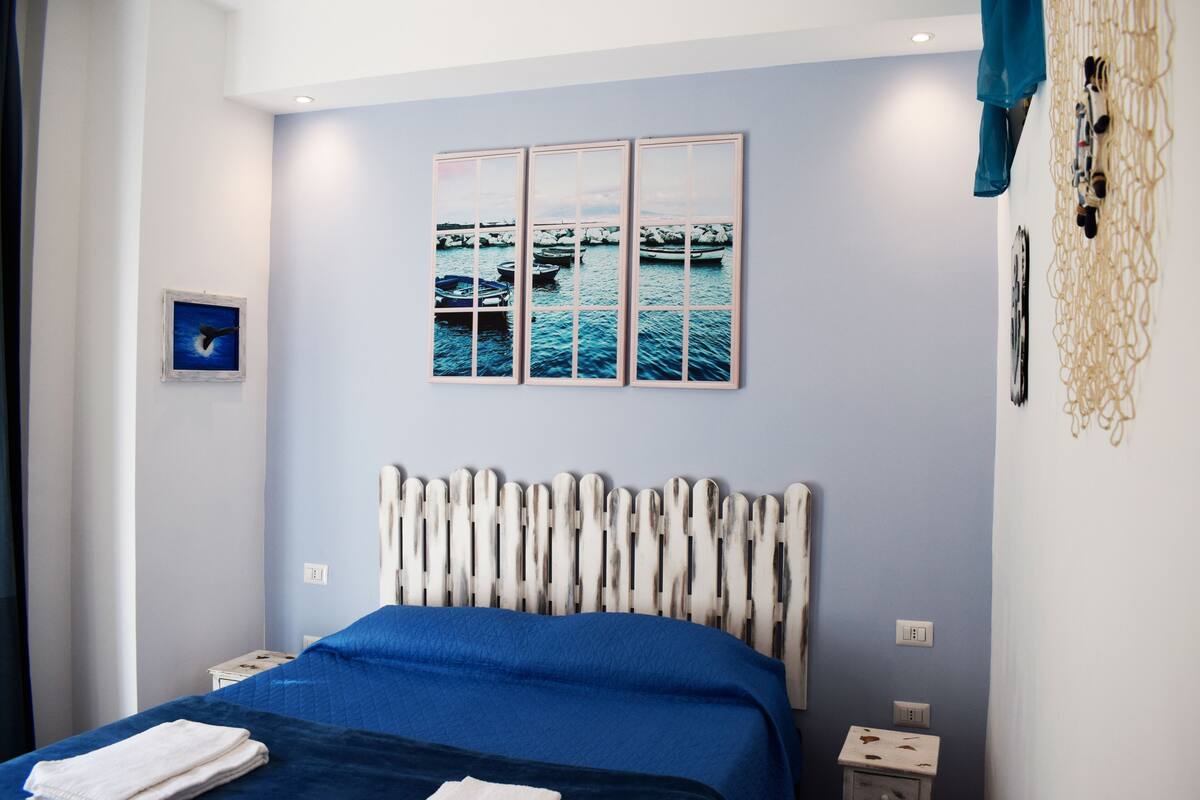 Quarto com cama, cabeceira, mesa de cabeceira e uma obra de arte na parede.