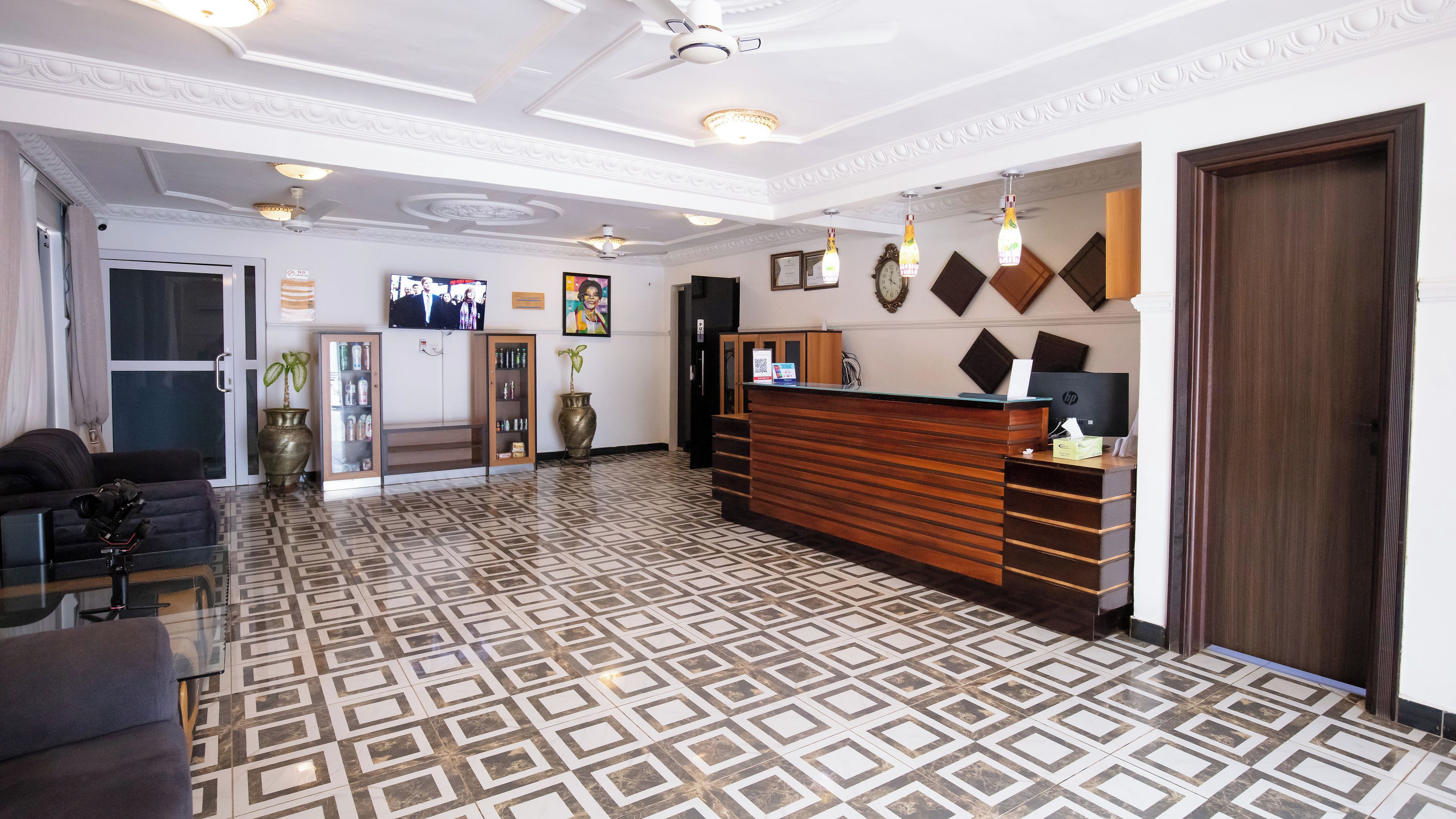 A hotel reception area with a patterned floor, a reception desk, a television, and a clock on the wall.
