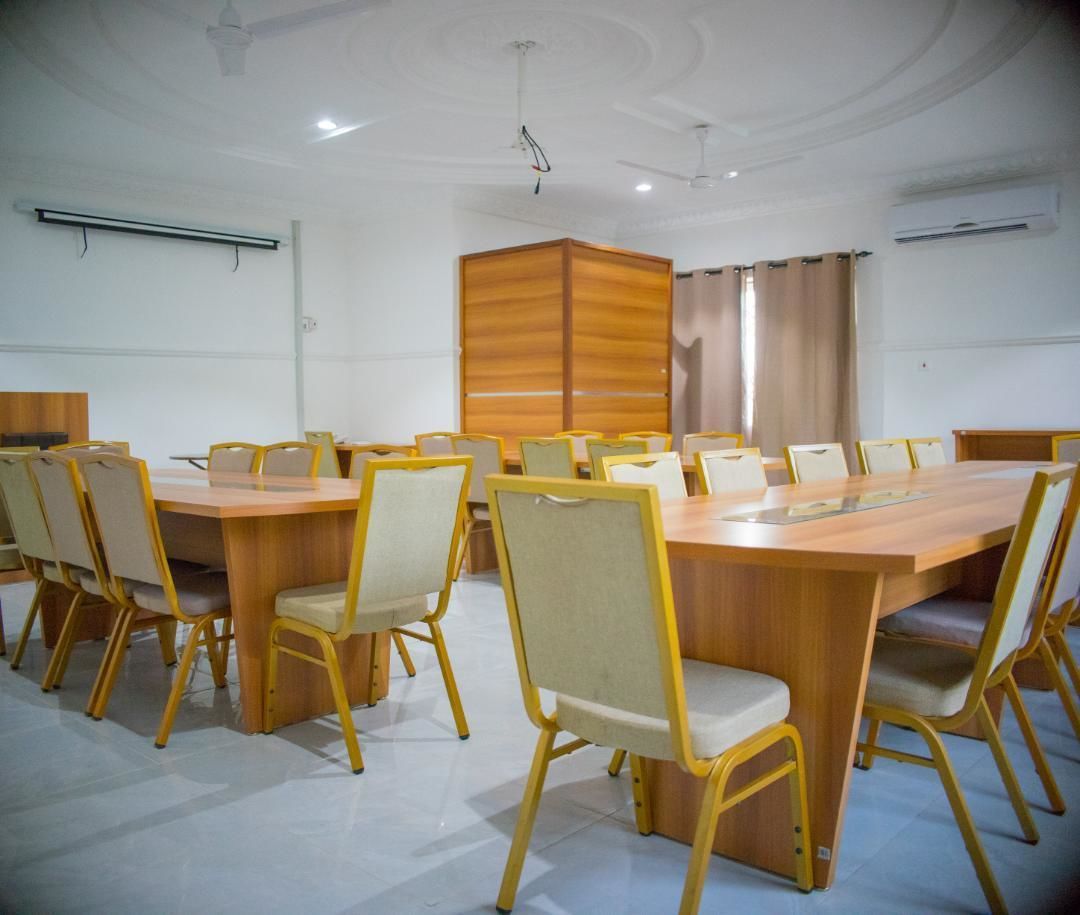 Ein Konferenzraum mit einem großen Holztisch, umgeben von Stühlen, einem Projektor und einer Whiteboard-Wand.