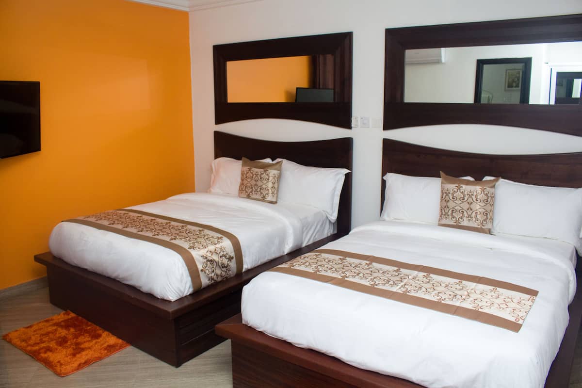 Habitación de hotel con dos camas, cada una con cabecera, un televisor de pantalla plana montado en la pared y una pared de acento marrón.