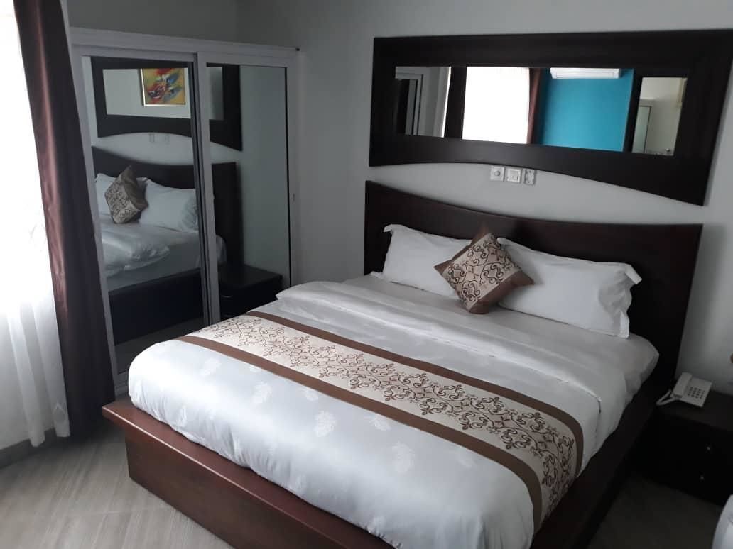A neatly made bed with a patterned bedspread, a bedside table with a phone, and a mirror above the bed.