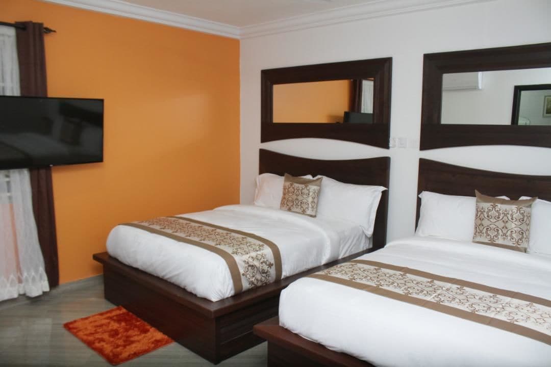 Habitación de hotel con dos camas, un televisor montado en la pared y una alfombra roja en el suelo.