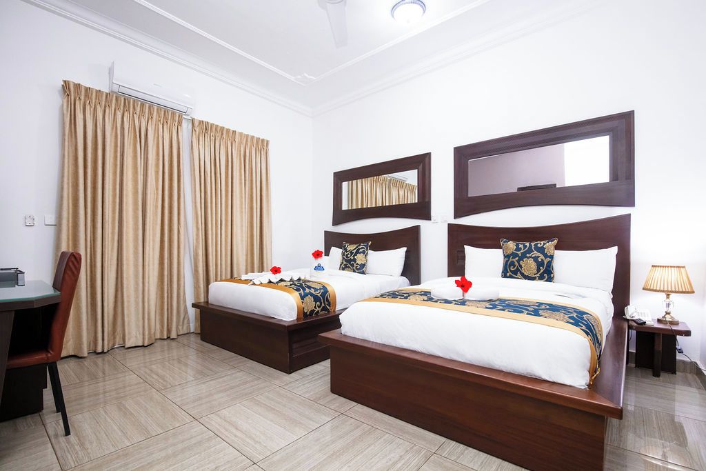 A hotel room with two beds, a desk, a chair, and a lamp.