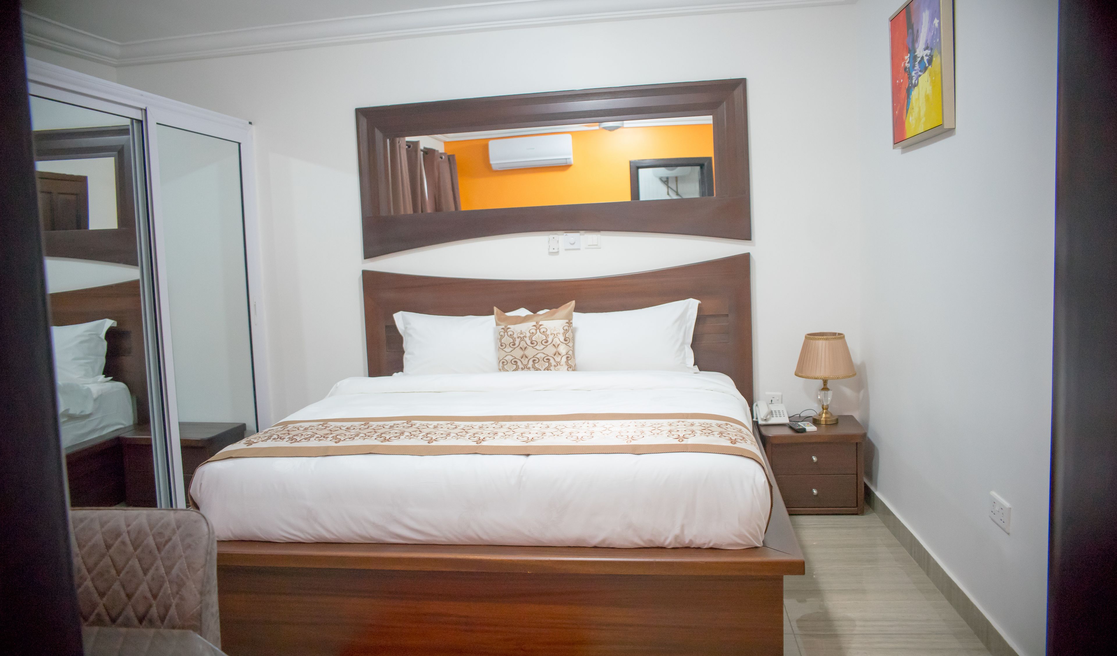 Una camera d'albergo con un letto grande, un comodino con una lampada e uno specchio sopra il letto.