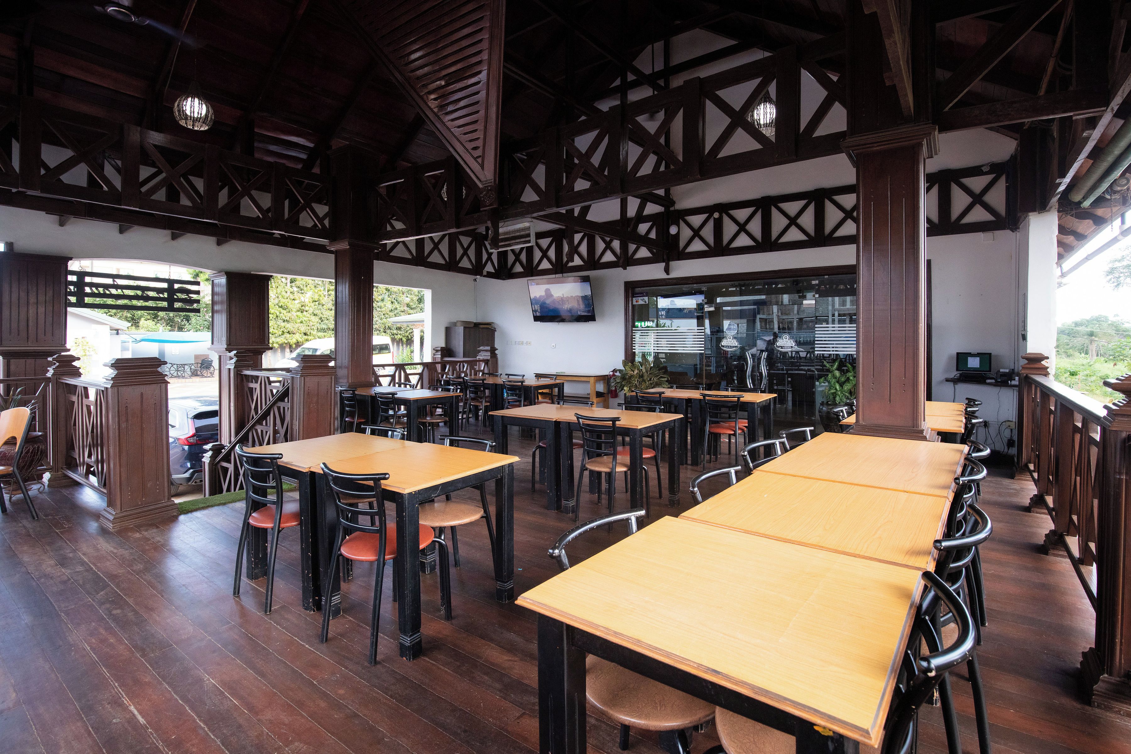 A restaurant with wooden tables and chairs, a high ceiling with exposed beams, and a view of the outdoors.