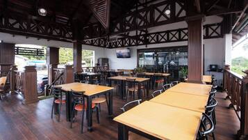 A restaurant with wooden tables and chairs, a high ceiling with exposed beams, and a view of the outdoors.