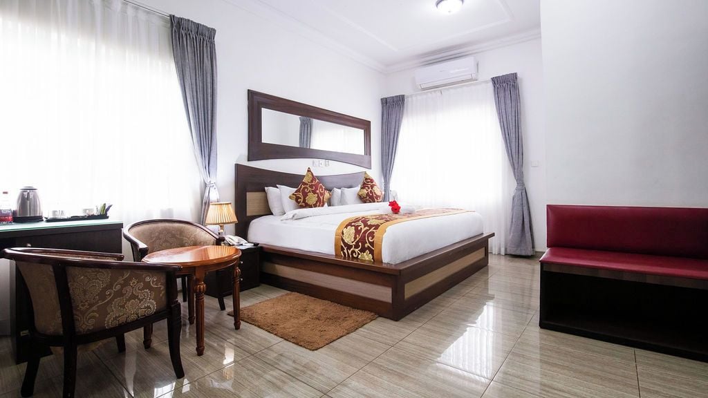 Habitación de hotel con cama, escritorio, silla, sofá y ventana con cortinas.