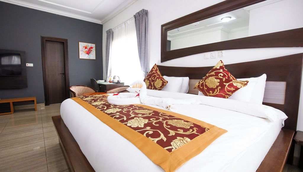 Una habitación de hotel con una cama grande, una mesita de noche, una silla, un escritorio y una televisión.