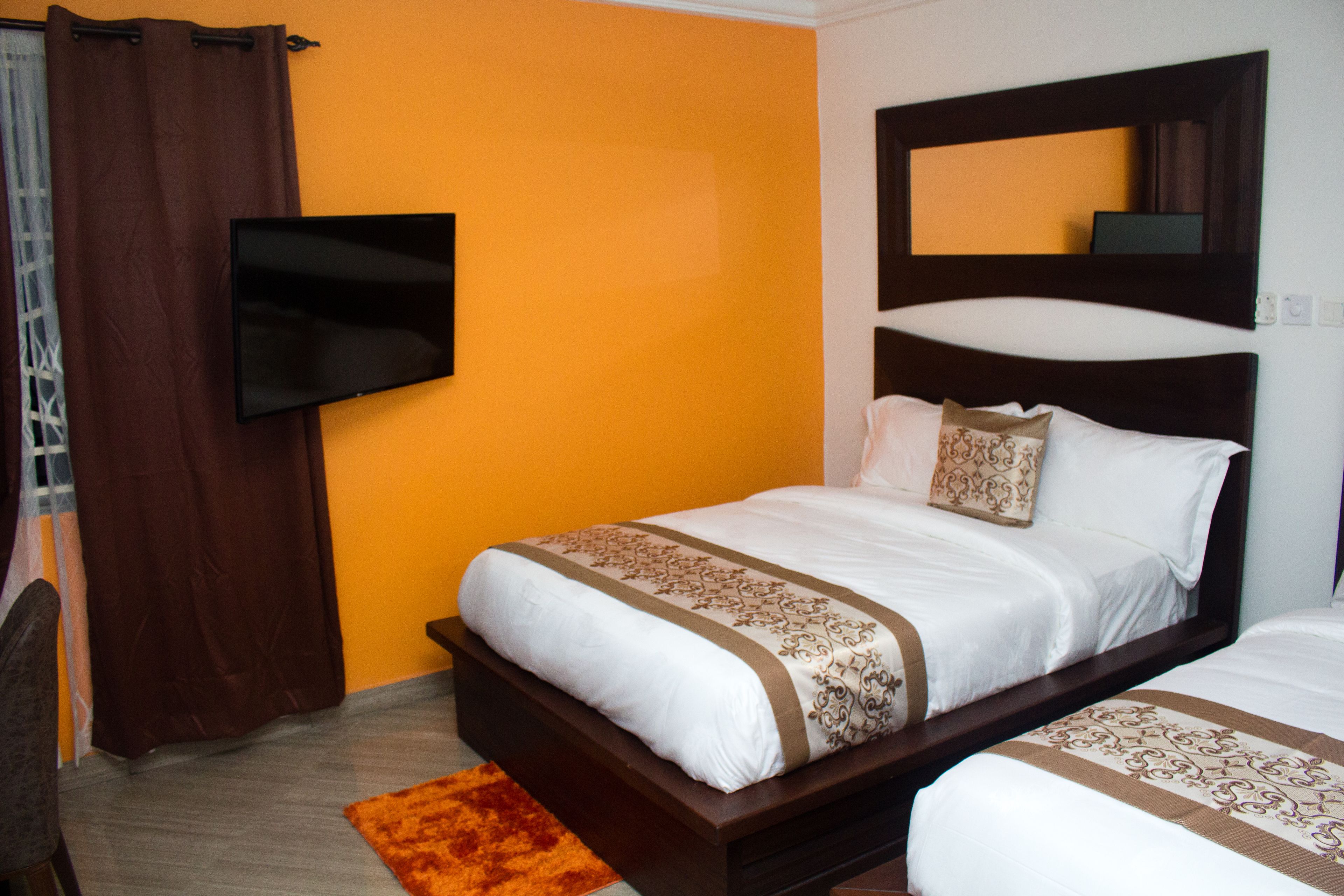 A hotel room with a single bed, a TV mounted on the wall, and an orange accent wall.