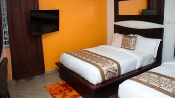 A hotel room with a single bed, a TV mounted on the wall, and an orange accent wall.