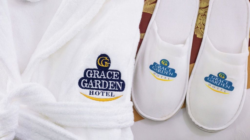 Ein weißer Bademantel und ein Paar weiße Hausschuhe mit aufgestickten Logos des Grace Garden Hotels.