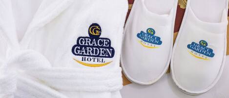 Ein weißer Bademantel und ein Paar weiße Hausschuhe mit aufgestickten Logos des Grace Garden Hotels.