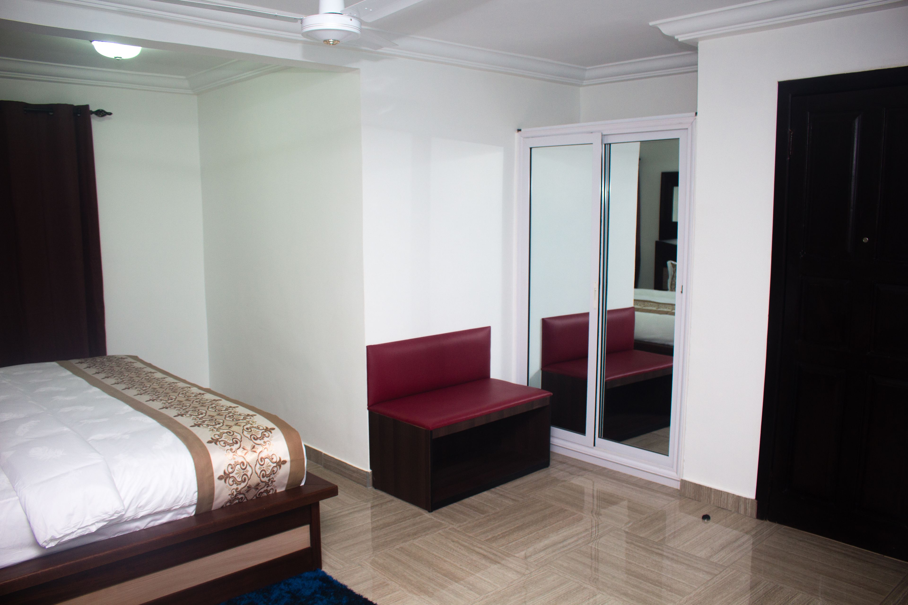 A bedroom with a bed, a red bench, a sliding glass door, and a dark door.