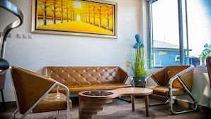 Een moderne woonkamer met een bruine leren bank, twee vleugelstoelen, een houten salontafel en een schilderij van een geel landschap aan de muur.