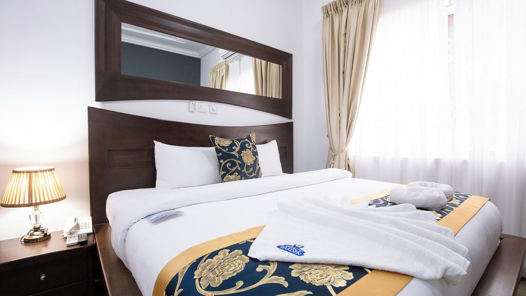 A hotel room with a large bed, a nightstand with a lamp, a mirror, and a window with curtains.