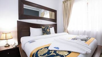 A hotel room with a large bed, a nightstand with a lamp, a mirror, and a window with curtains.