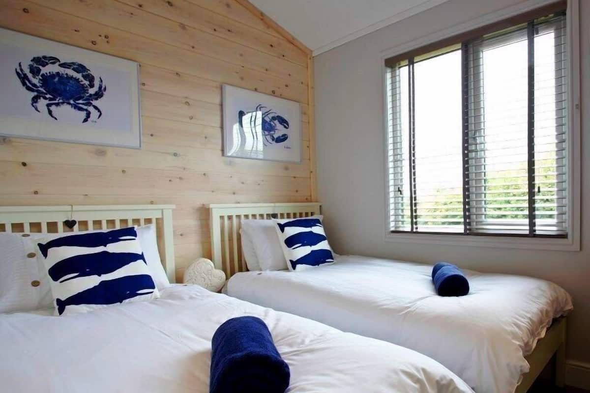 A room with two beds, wooden paneling on the walls, and a window with blinds.