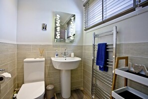 Un baño con inodoro, lavabo, espejo, toallero y estante con un letrero.