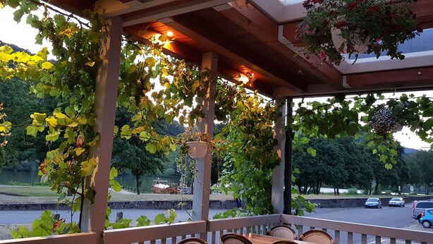 A covered outdoor seating area with a view of a lake and parked cars. - Hotel zum Anker (Neumagen-Dhron)