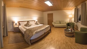 A hotel room with a wooden ceiling, a bed with patterned bedding, a green armchair, a round wooden side table, and a sofa. - Hotel zum Anker (Neumagen-Dhron)
