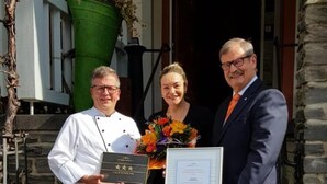 Three people standing outside a building, holding plaques. - Hotel zum Anker (Neumagen-Dhron)