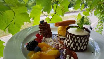 Ein Desserteller mit verschiedenen Früchten und Schokolade auf weißem Geschirr, draußen arrangiert mit grünen Blättern im Hintergrund.