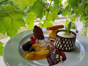 A dessert plate with various fruits and chocolate on a white plate, set outdoors with green leaves in the background. - Hotel zum Anker (Neumagen-Dhron)