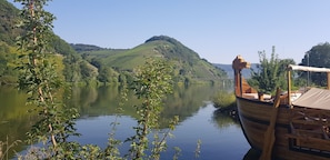 A wooden boat docked at a calm river with a forested hill in the background. - Hotel zum Anker (Neumagen-Dhron)