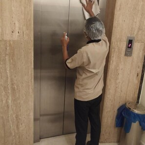 A person cleaning a metallic elevator door in a room with a marble wall and a digital display showing the number 2. - Hotel Picasso (New Delhi)
