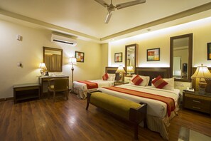 A hotel room with two beds, a desk, a chair, a bench, and a ceiling fan. - Hotel Picasso (New Delhi)