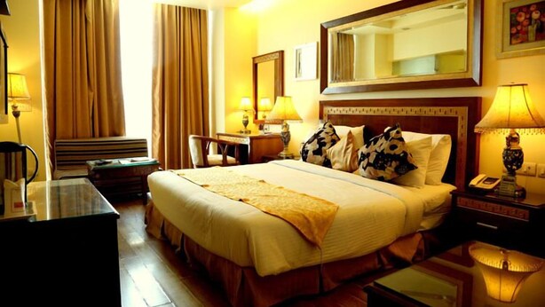 A hotel room with a large bed, a desk, a chair, a nightstand, and a mirror. - Hotel Picasso (New Delhi)