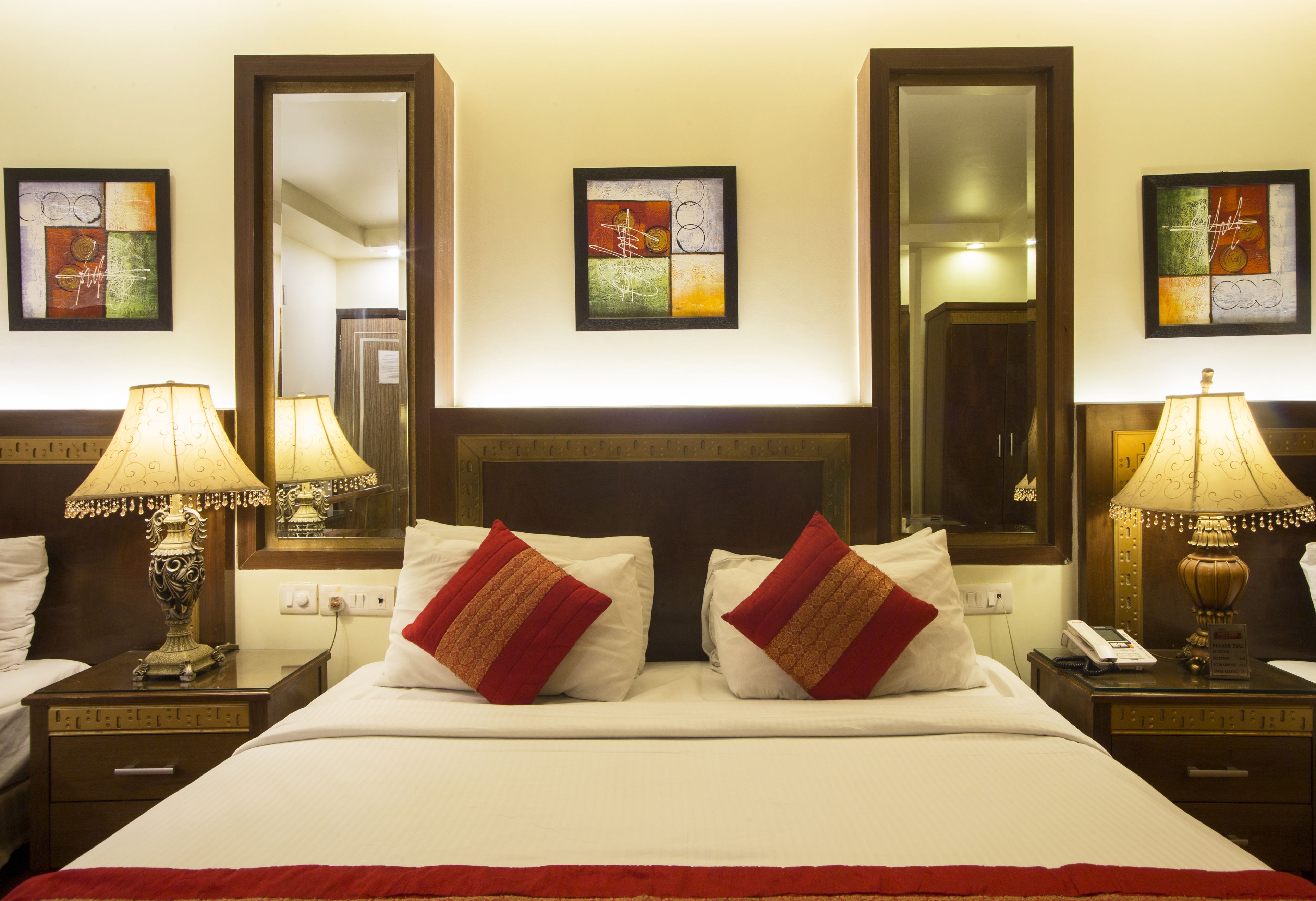 A hotel room with a large bed, two bedside tables with lamps, a mirror above the bed, and artwork on the walls.