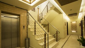 A hotel lobby with a marble floor, a staircase with metal railings, an elevator, and a trash can. - Hotel Picasso (New Delhi)
