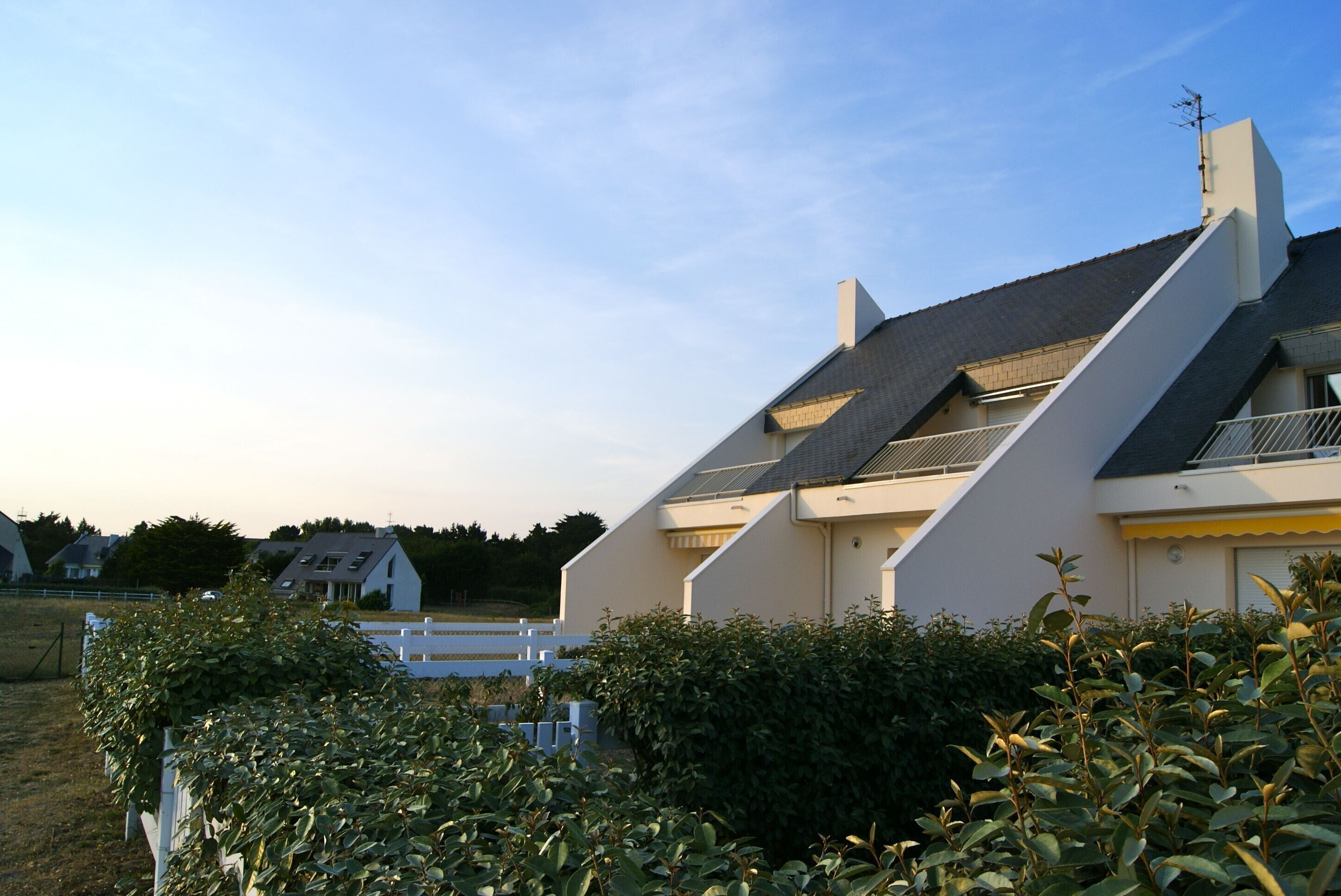 Una casa moderna con techo inclinado, paneles solares y cerca blanca.