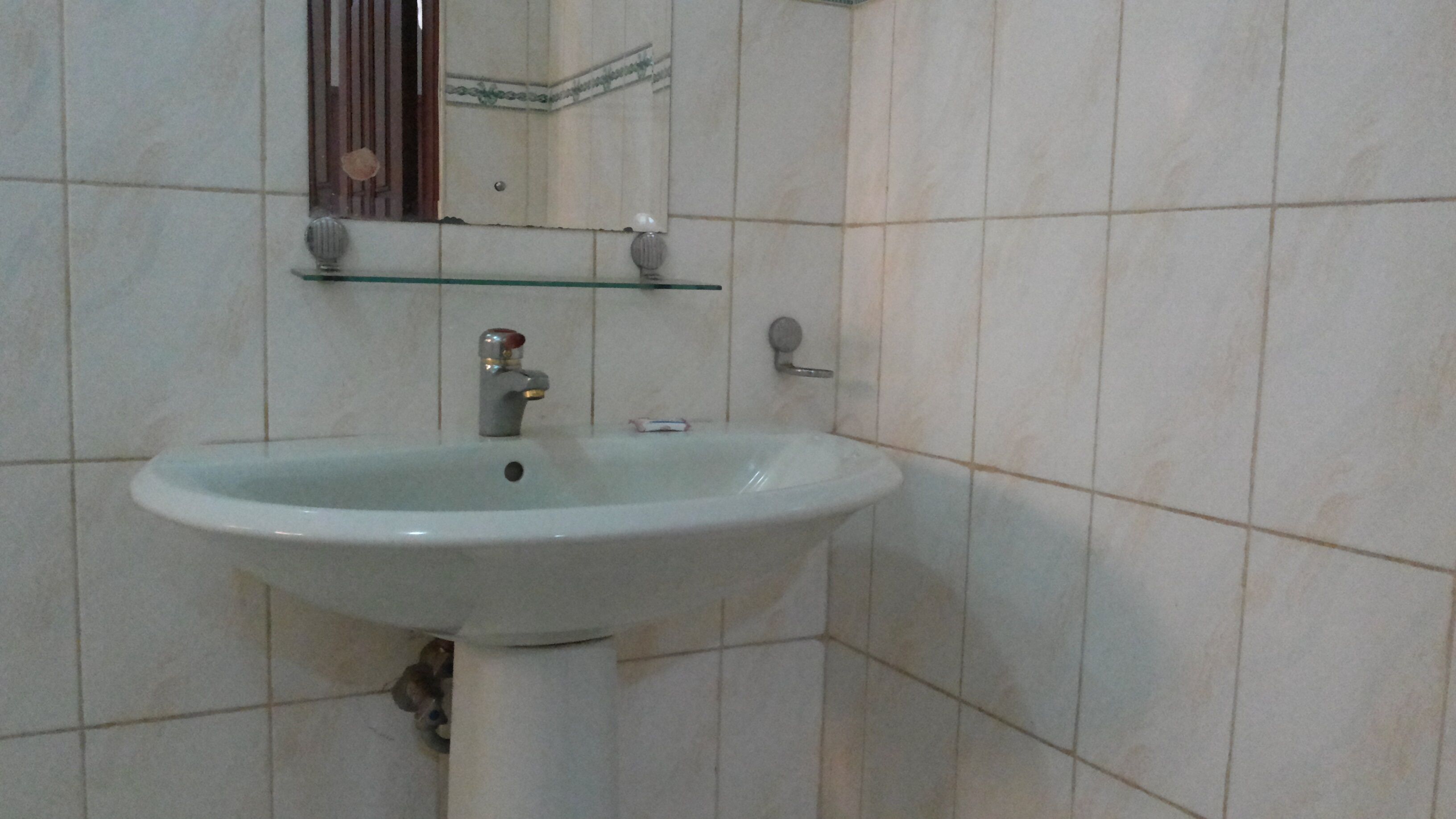 A bathroom with a white sink, a mirror, and a glass shelf above the sink.