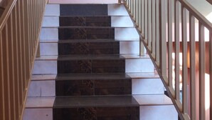 Un escalier dont les marches alternent entre des couleurs foncées et claires, avec des rampes en métal et un panneau indiquant le premier étage.