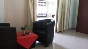 Une pièce avec un fauteuil noir, une petite table recouverte d’une nappe rouge et une plante en pot.