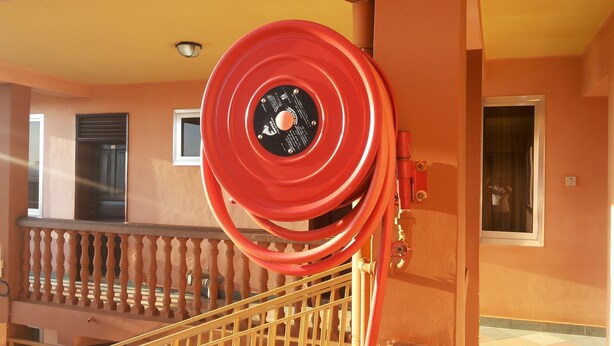 Un tuyau d’incendie rouge est enroulé contre un bâtiment doté d’un balcon et de fenêtres.