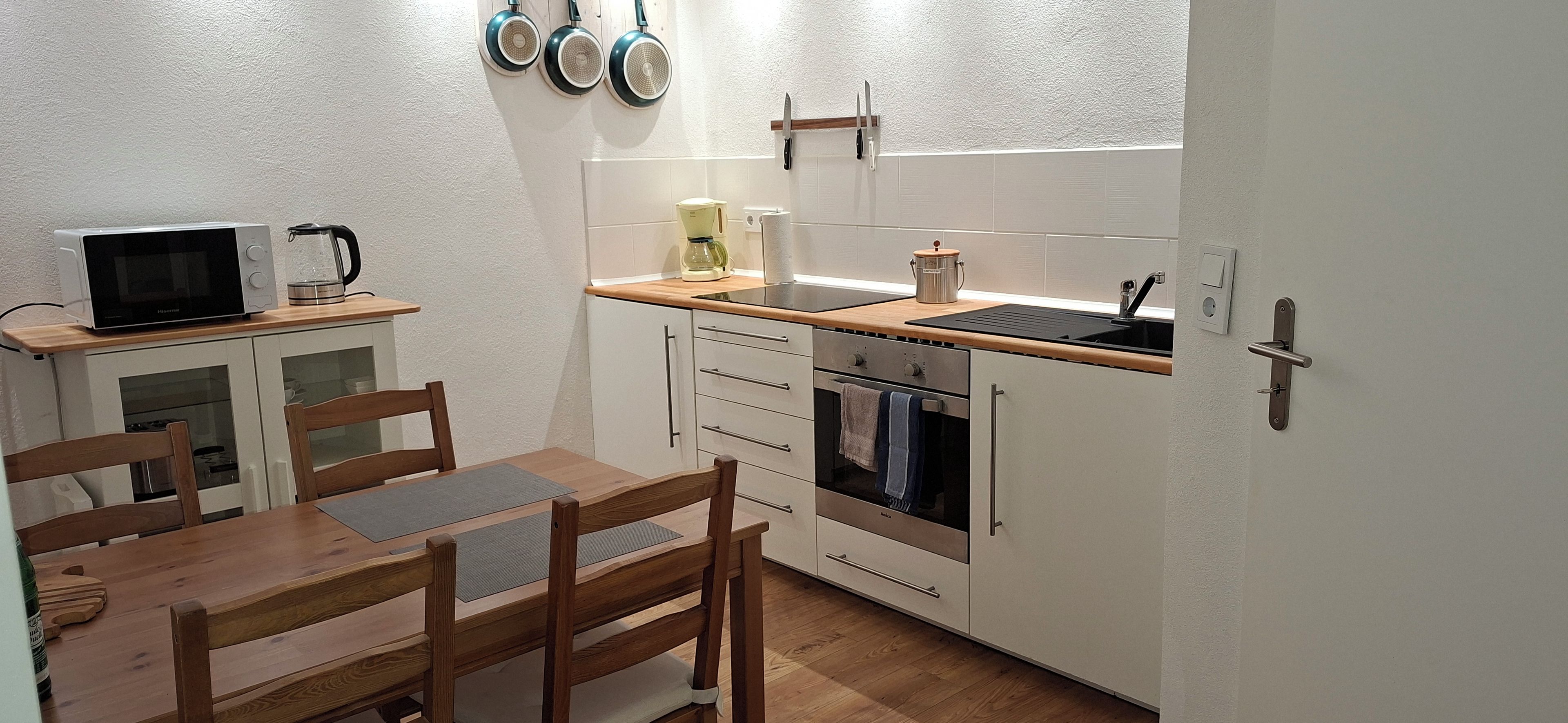 A compact kitchen with a microwave, kettle, and kettle on the countertop. There is a wooden dining table with chairs.