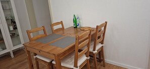 A wooden dining table with four chairs, a placemat, and two bottles on the table.