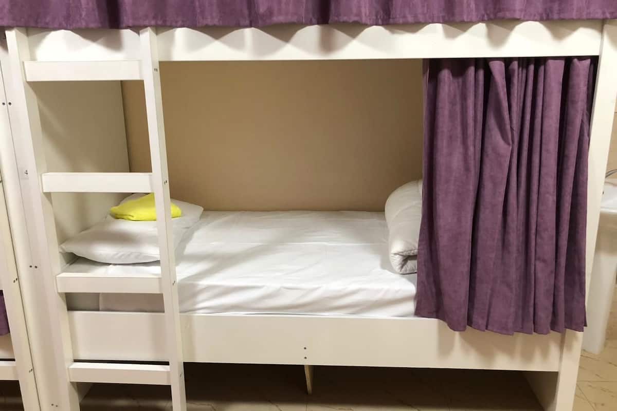A bunk bed with a ladder, white bedding, and a purple curtain.